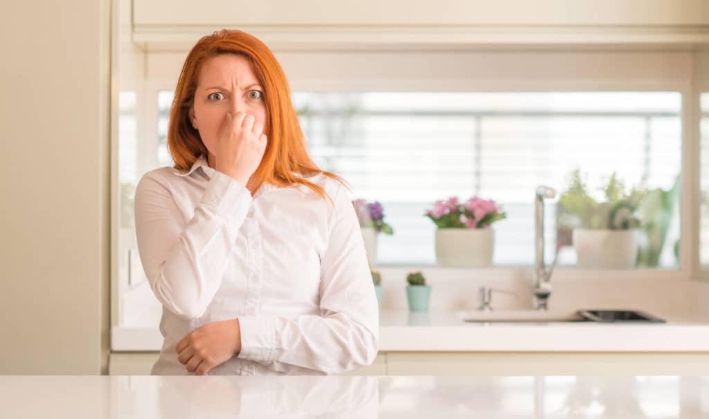 A woman standing in the kitchen plugging her nose